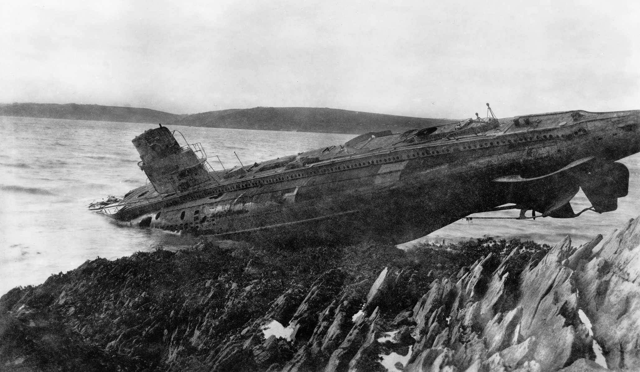A black and white archive image of a submarine stranded on a rocky coast.