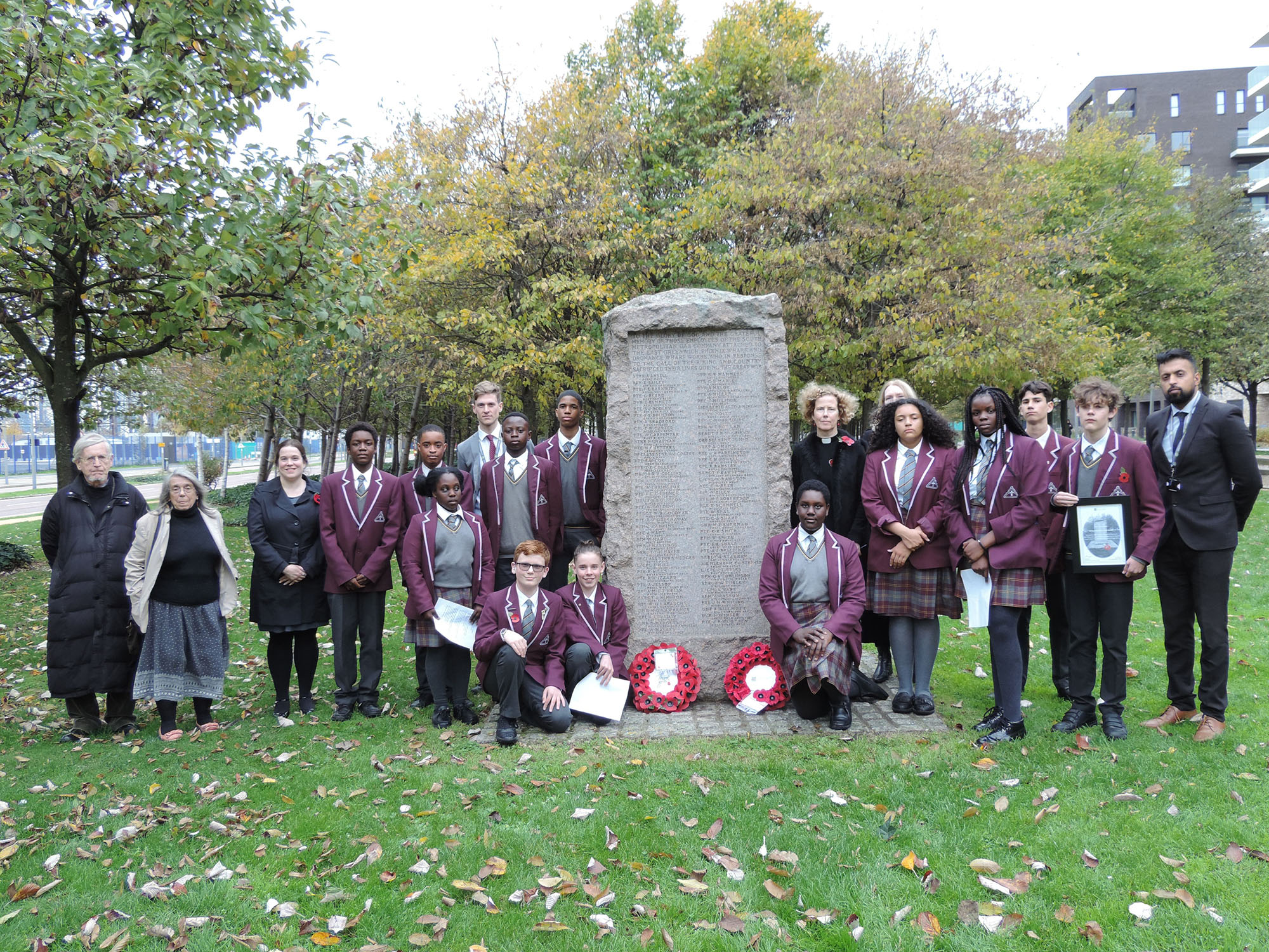 People standing around a war memorial with two poppy wreaths laid at the base of it