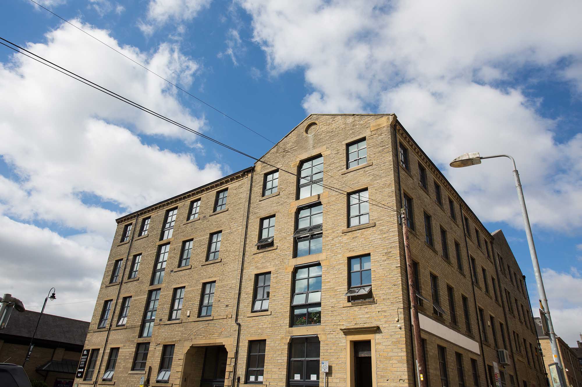 A yellow brick office building with many windows against a blue cloudy sky
