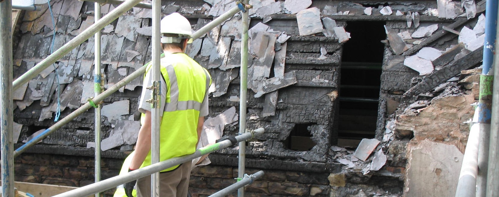Man in high viz and hard hat standing on scaffolding examining roof damaged by fire
