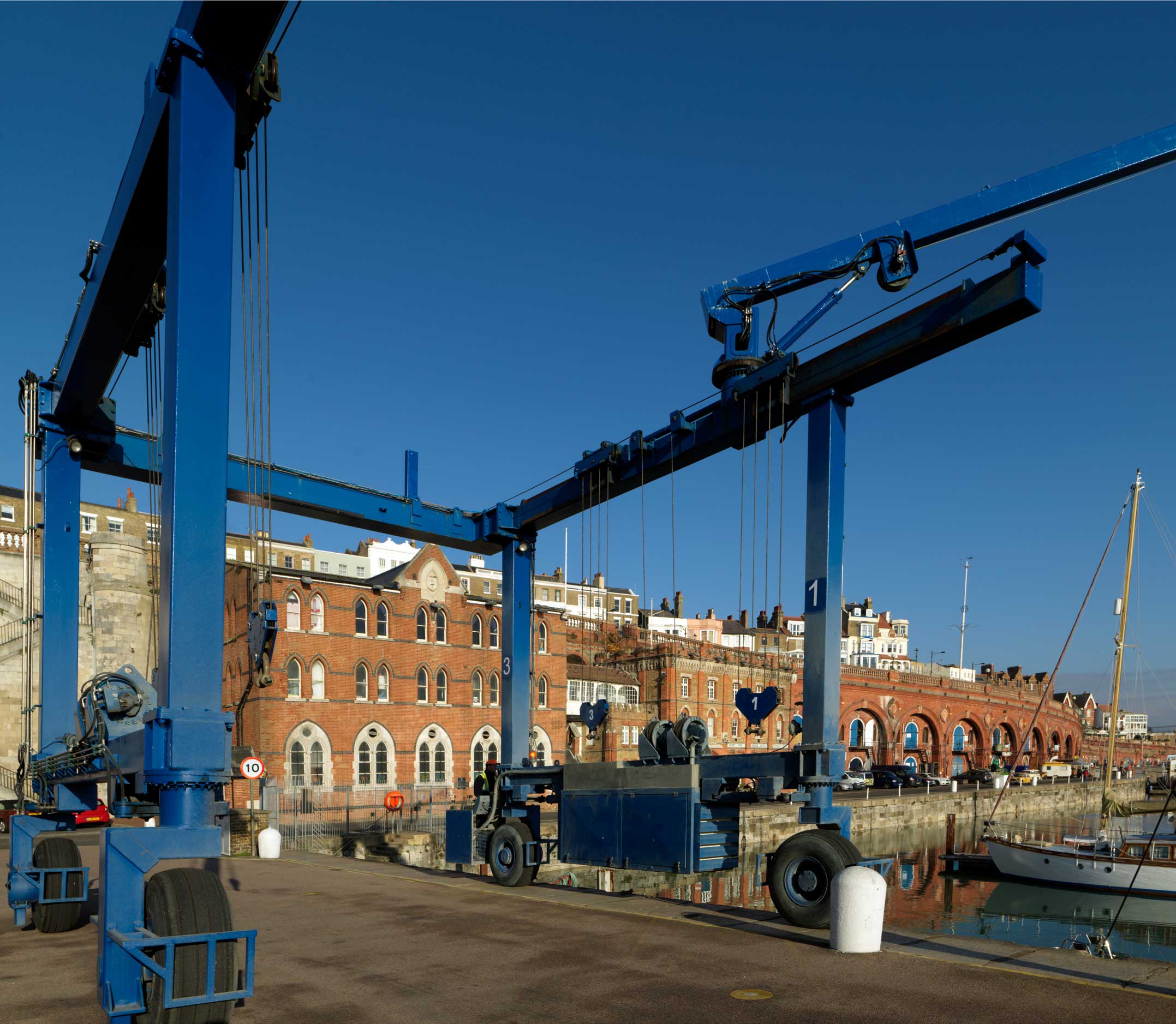 A view of a harbour with buildings, a large crane and a small yacht.