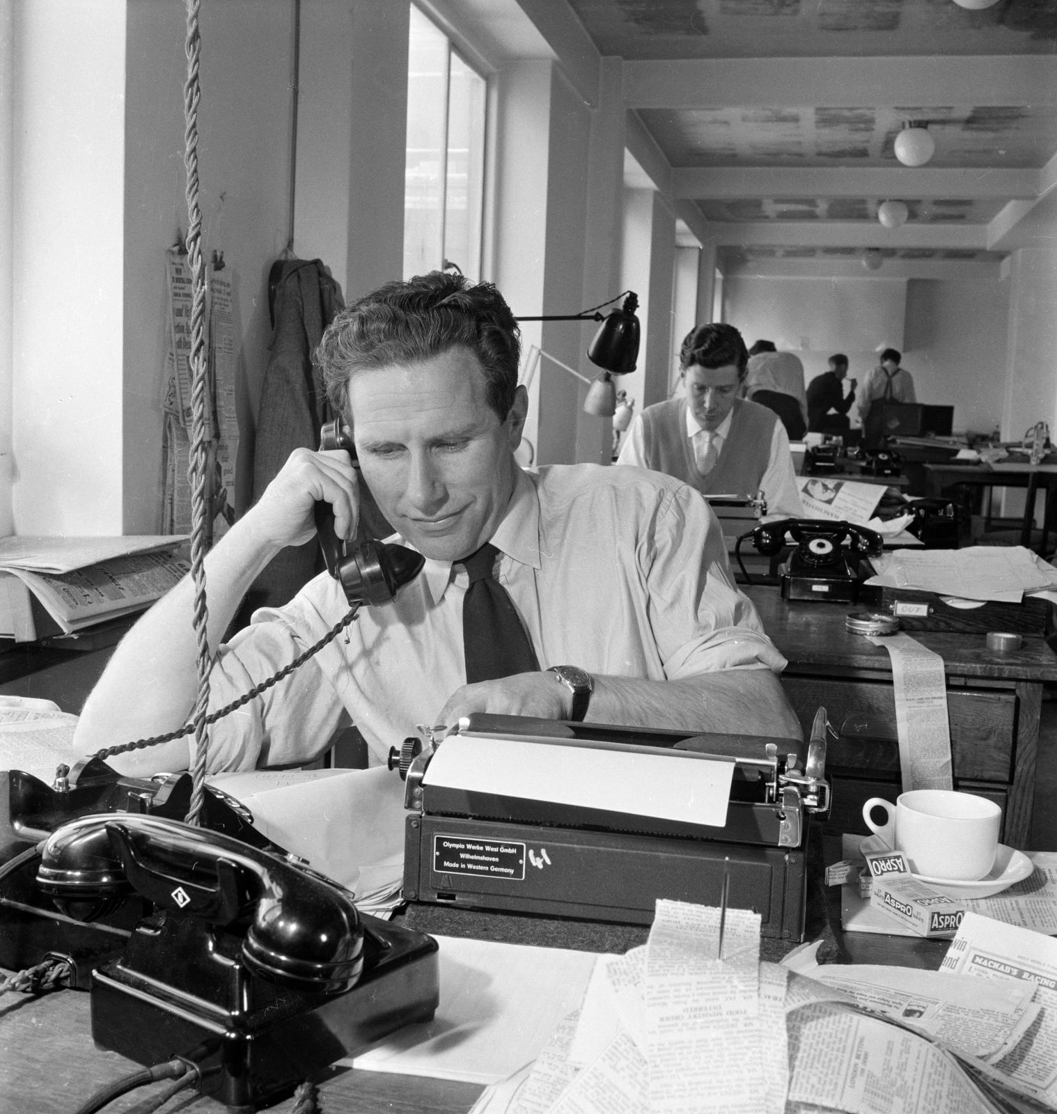 A newspaper office in 1955 with journalists sitting at their typewriters or on the phone.