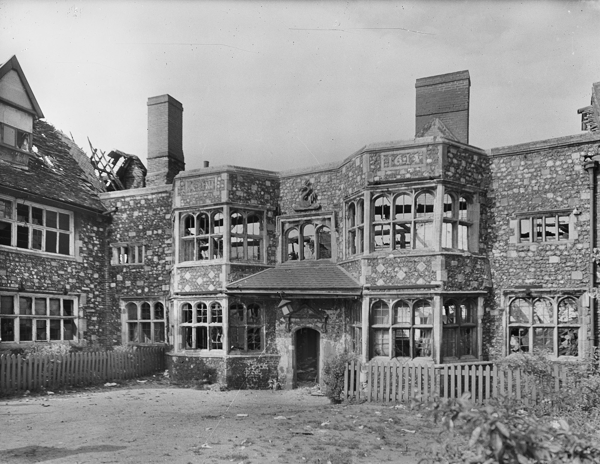 Large stone building with all window glass blown out and roof damaged.