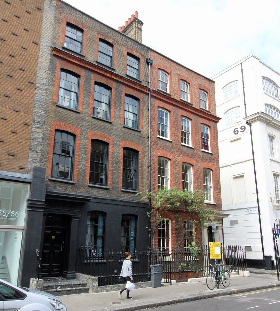 Georgian buildings with railings in front of them. One has a plant growing up the wall and over the ground floor windows.