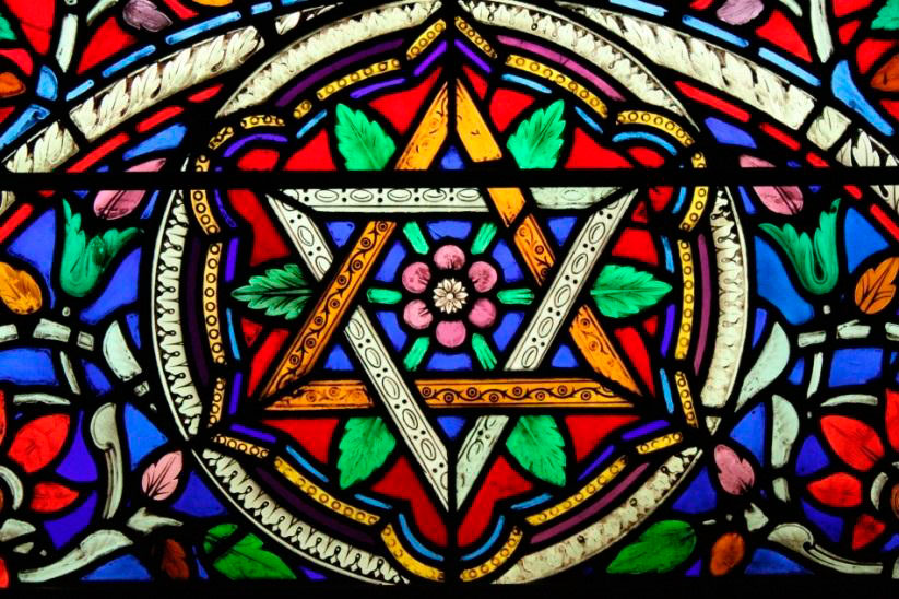 Stained glass window of a star shaped pattern with a flower in the centre and around the edges.
