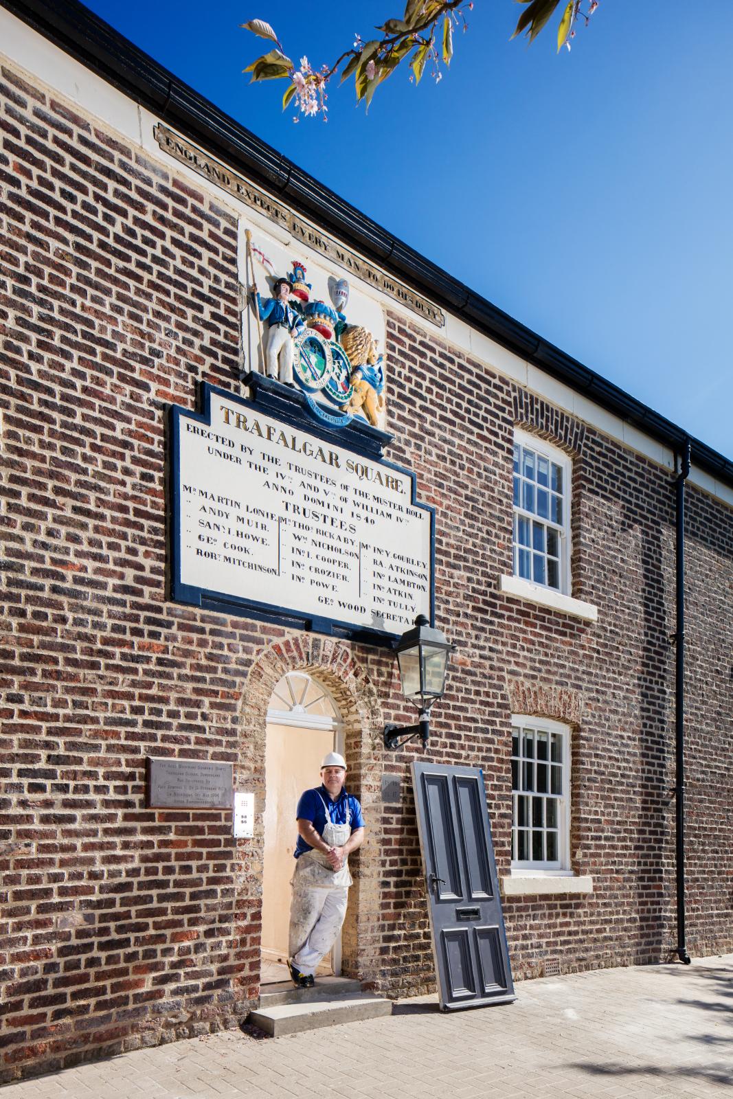 Workman standing in the doorway of the almshouses in Trafalgar Square.