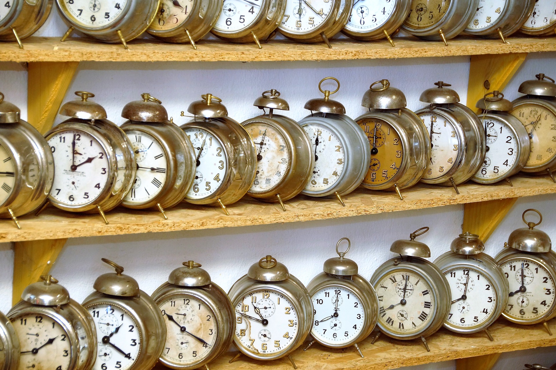 Image of old fashioned brass alarm clocks on wooden shelves.