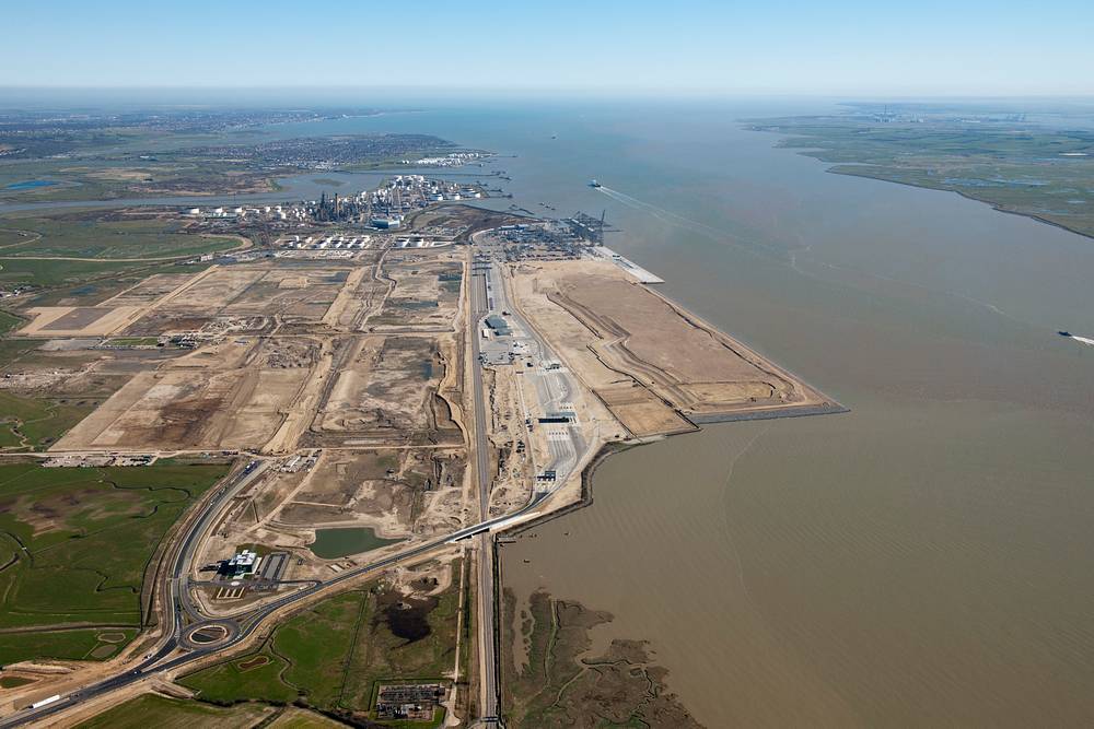 An oblique aerial colour photo of a London Gateway development, to the right is a large silty river, to the left a large industrial area.