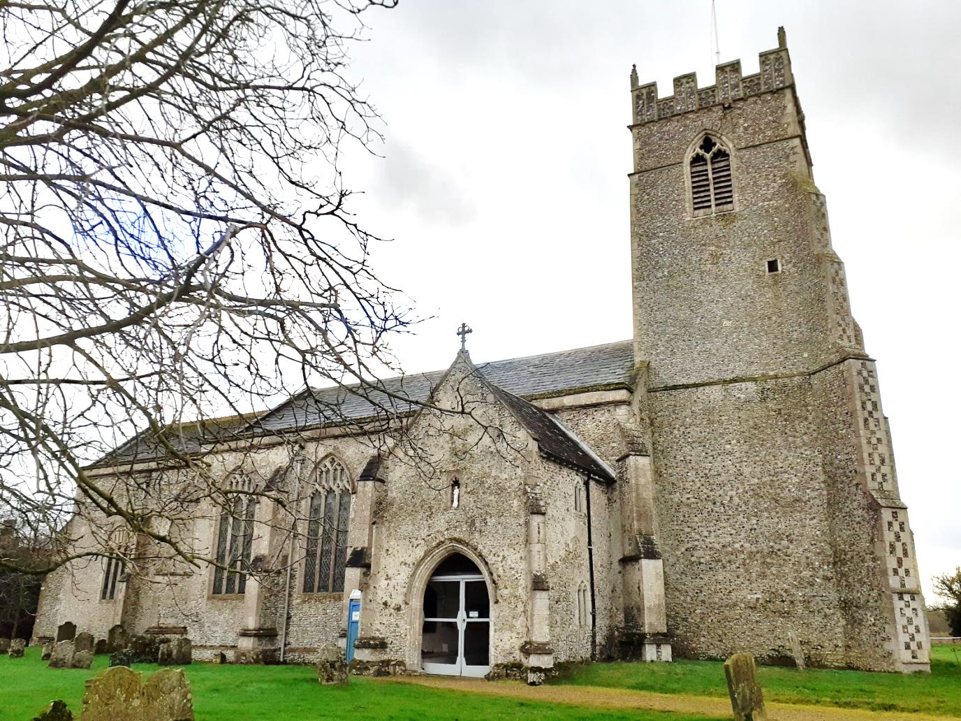 St Mary's Church North Tuddenham, a medieval stone church sitting in grassland with trees in the foreground.