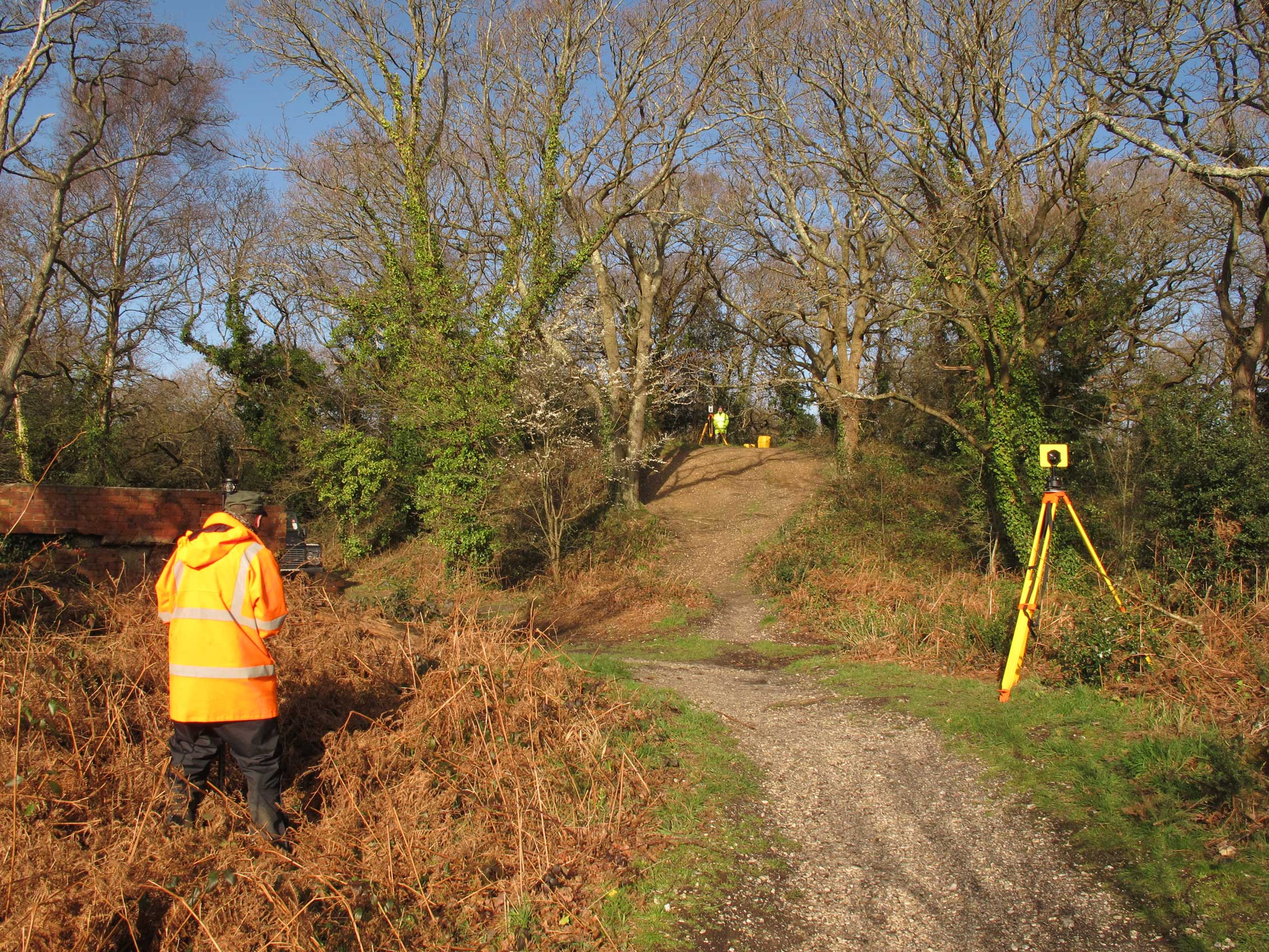 Two archaeologists in hi-vis gear surveying a small motte and bailey castle.