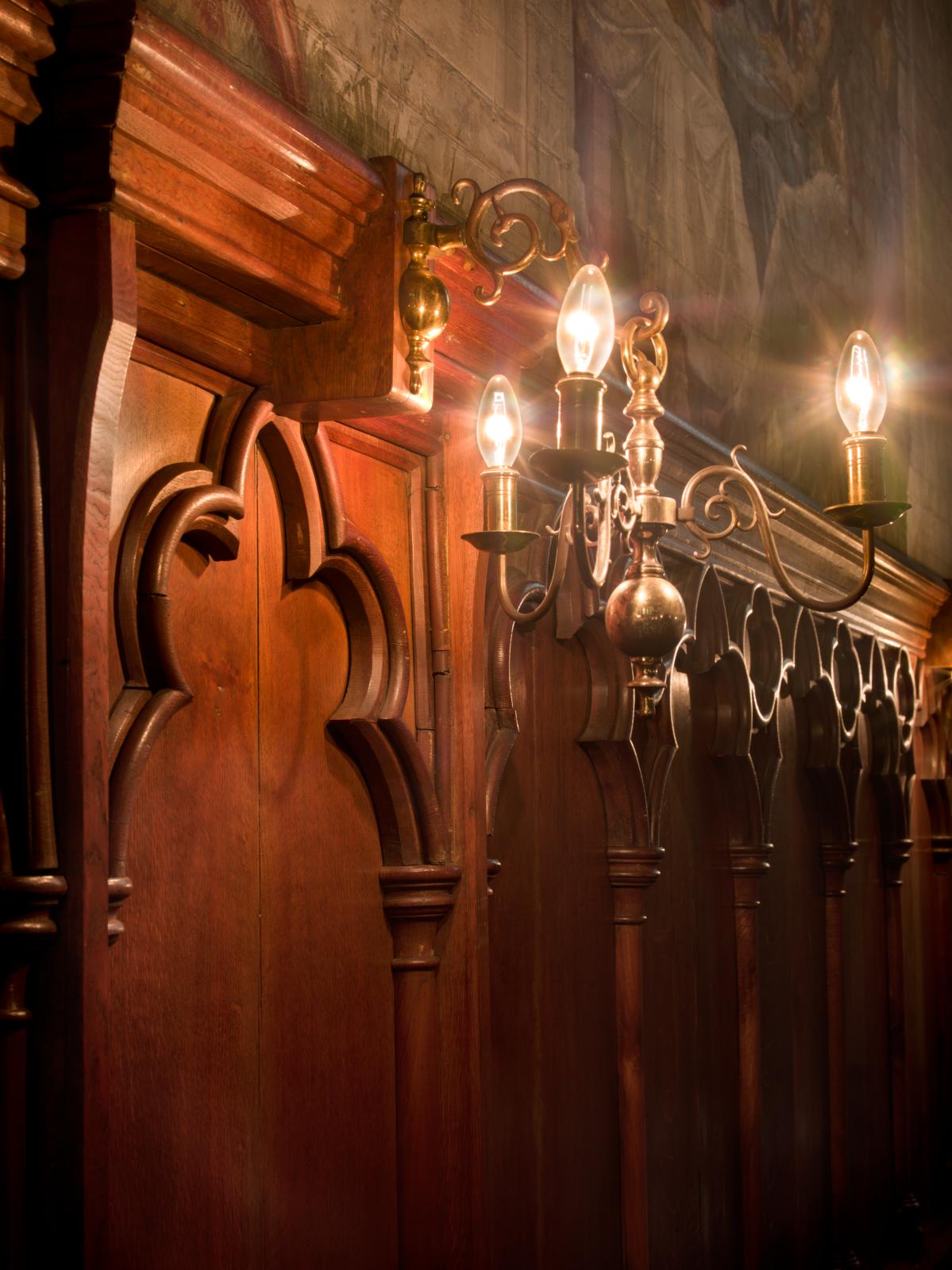 a lighting feature in a chapel. There is dark wooden paneling below the feature and a wall painting just above it