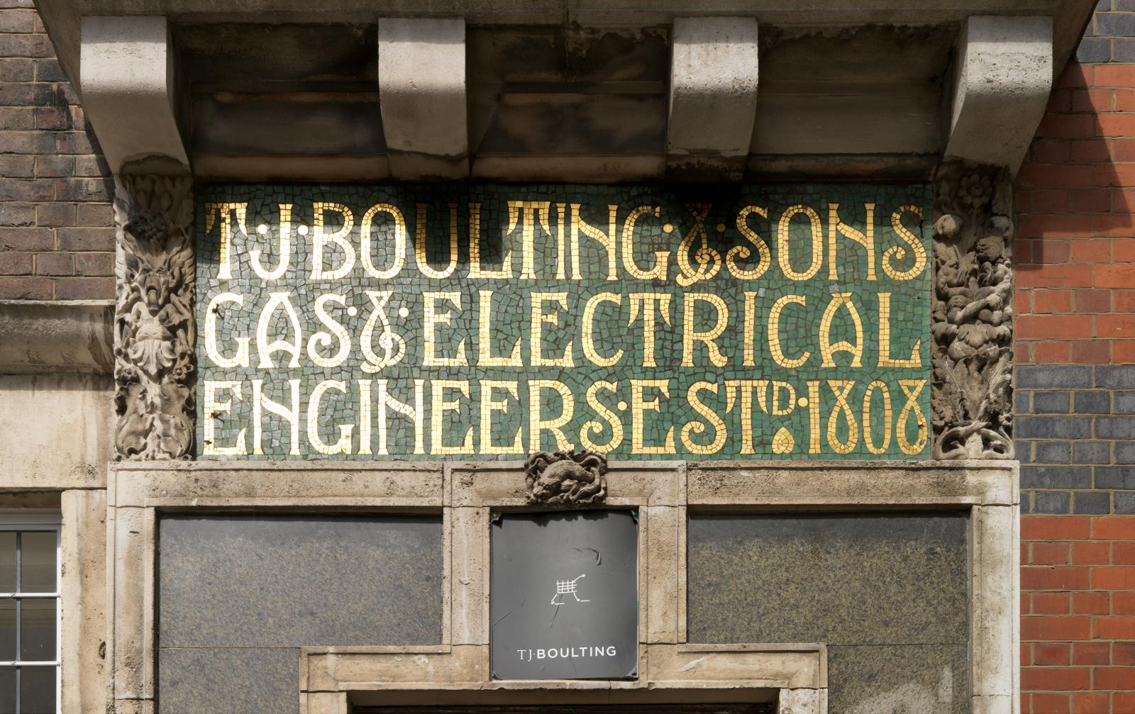 Signage in gold letters with green background. The signage is surrounded by brickwork and other architectural features