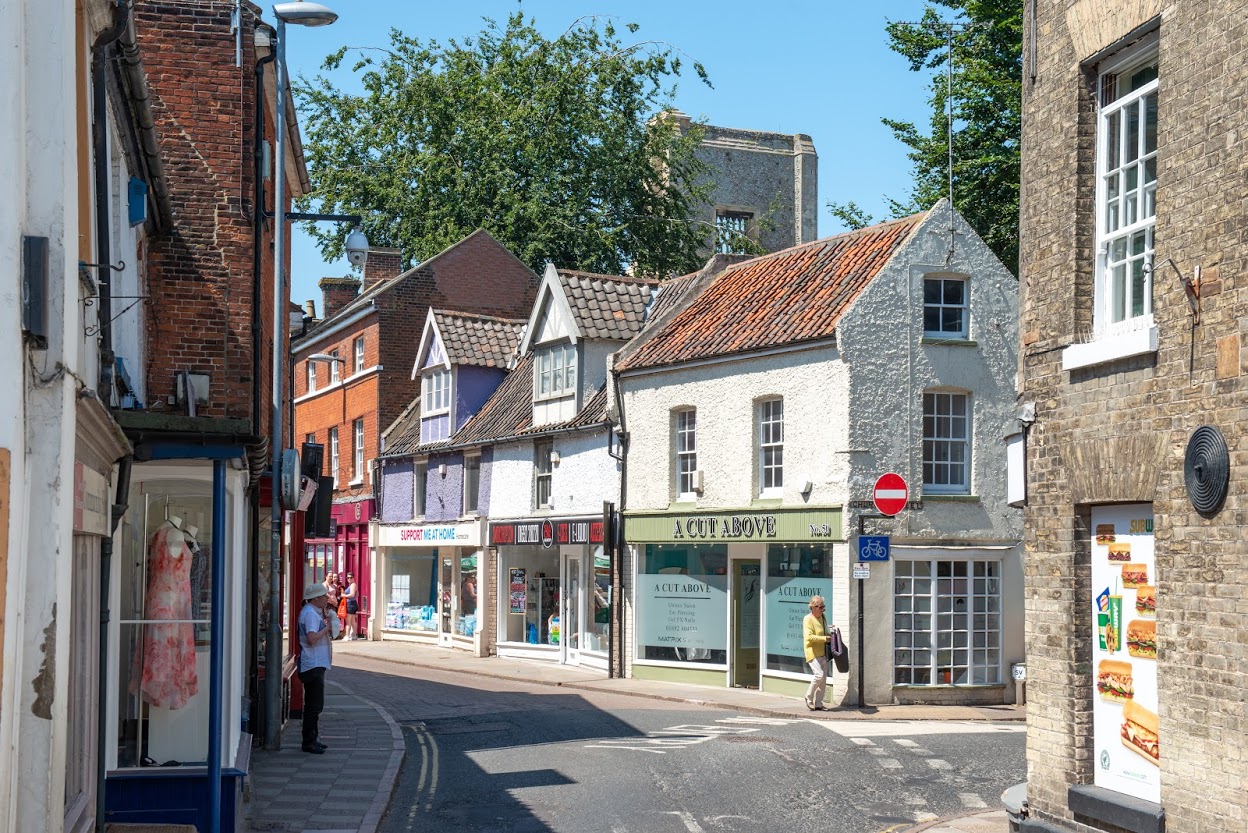 A winding lane with shops of different architecture shown across a curved street and a church in the background.