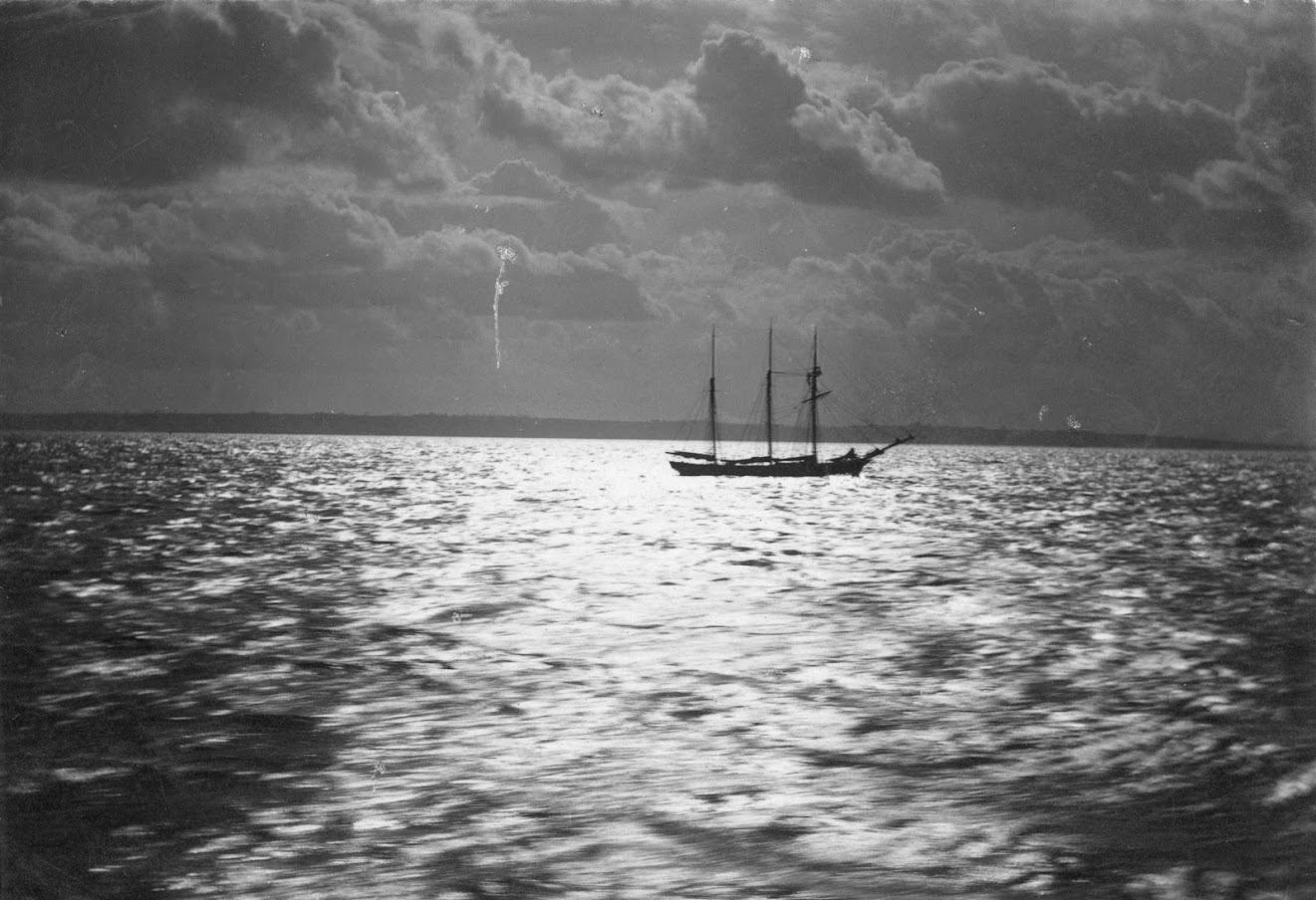 The moonlight shining on the river Thames at the estuary mouth, illuminating a three masted sailing ship and the coastline beyond.