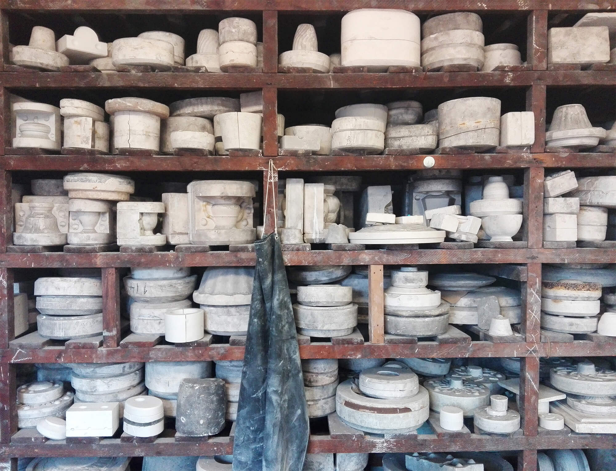 Photograph of shelves in a workshop stacked with plaster moulds for casting tableware ceramics. Varying sizes of moulds for teapots, bowls and cups are on display.