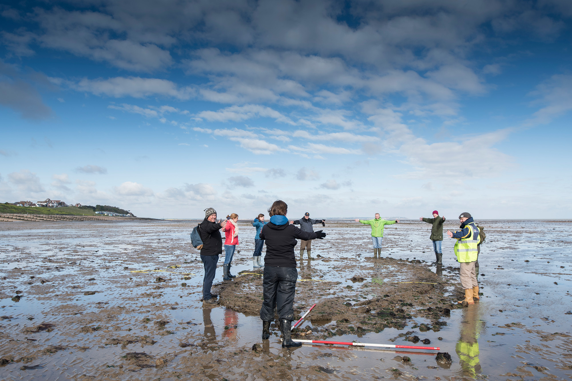 A group of people stood on a wet sandy beach forming a circle.