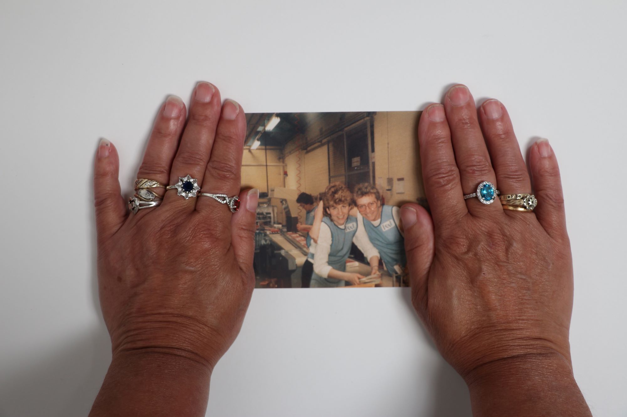 A photo showing hands holding a printed photograph of women at work in the 1980s. 