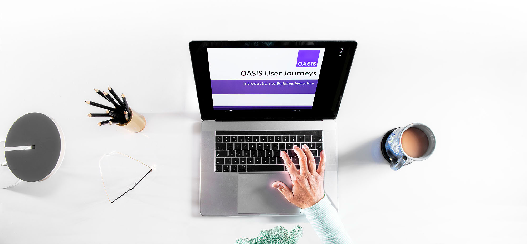 Detail of a desk with laptop displaying a remote training session,  a person's hand is poised on the keypad.