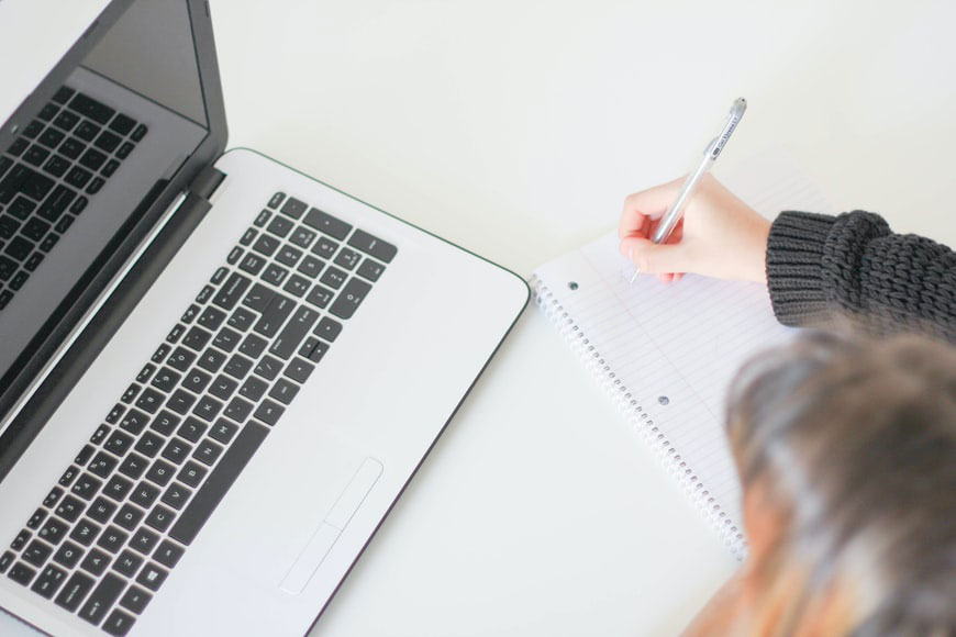 A woman writing notes on a pad with a laptop open in front of her.
