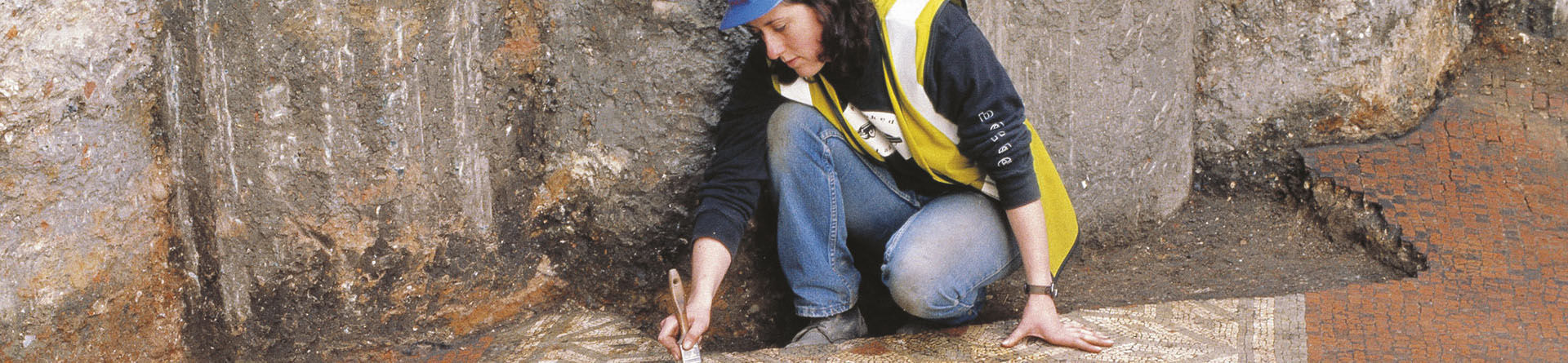 Archaeologist excavating mosaic next to foundation piles