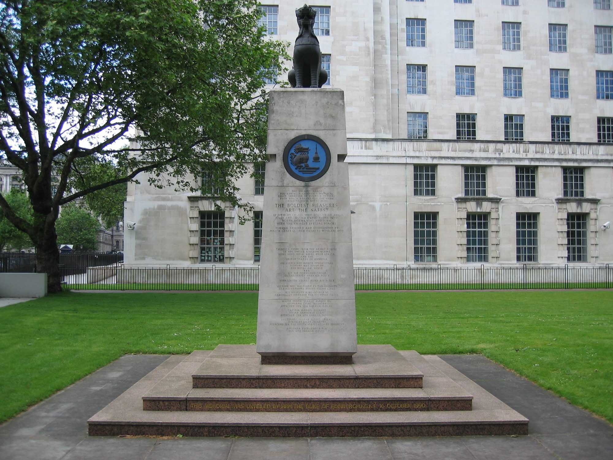 Stone tall column with bronze Burmese guardian temple creature (chindit) on top. Carved on stone are lists of units involved in the group blue enamel crest of the chindits association on front face