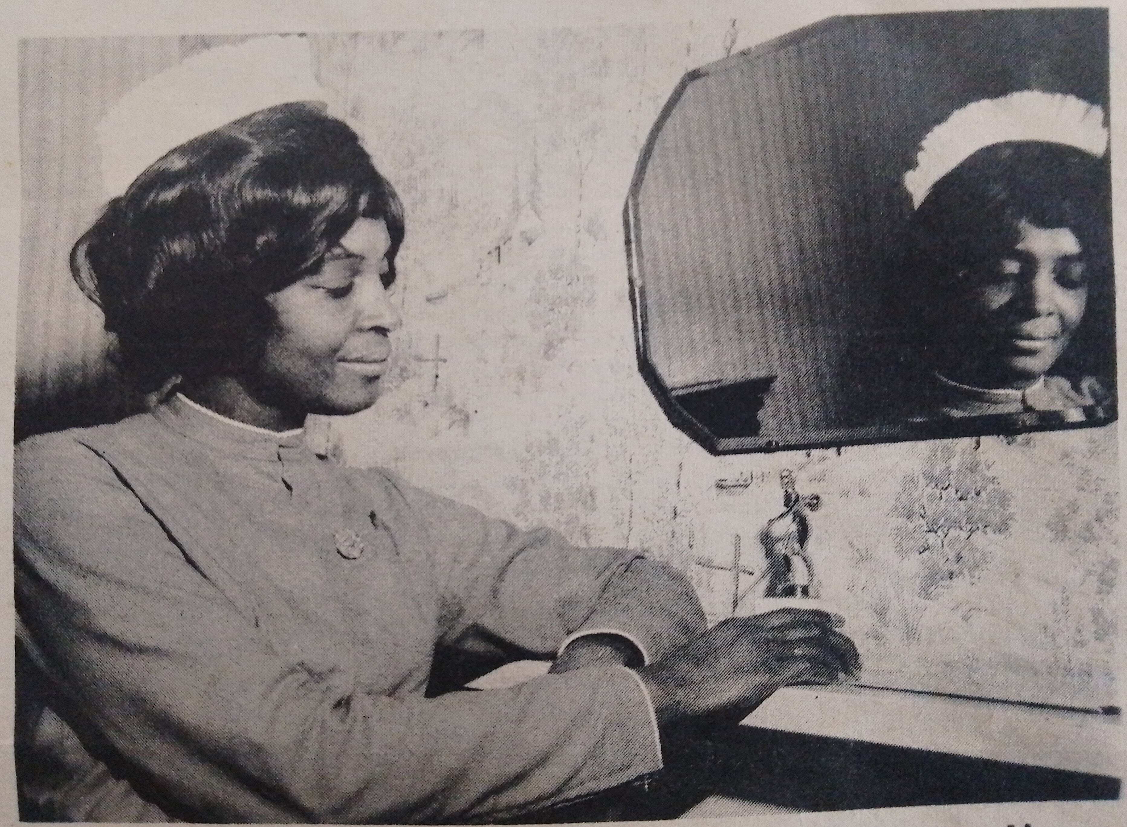 A black and white photo of a nurse posing by a mirror