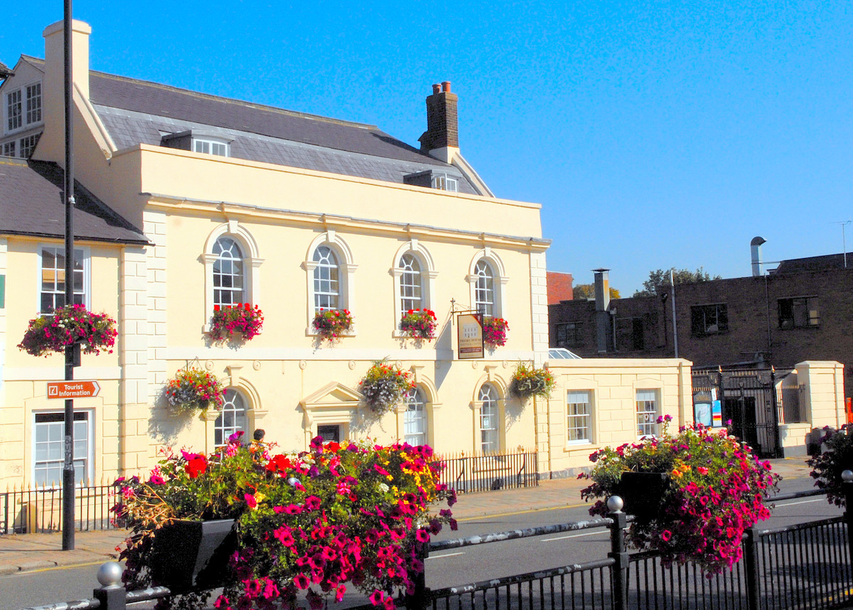 The image shows the exterior of Priory House with a butter yellow exterior paint and white around the window frames.