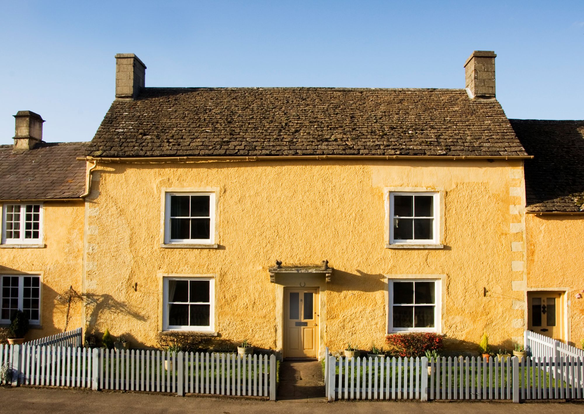 A photograph of the exterior of a traditional one-storey country cottage with a small fence surrounding the small front garden.