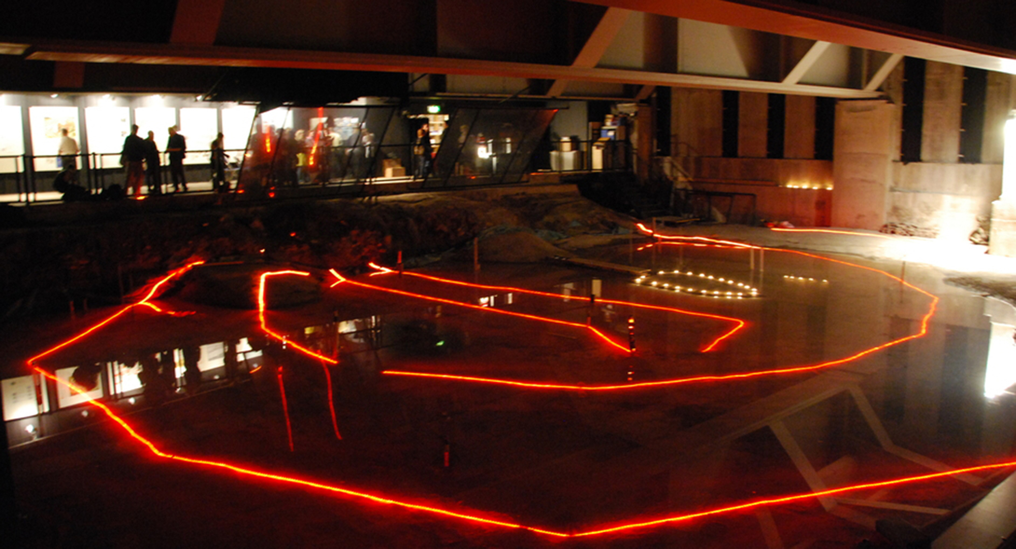 Red lighting shows the outline of archaeological remains of a building preserved beneath a modern development.