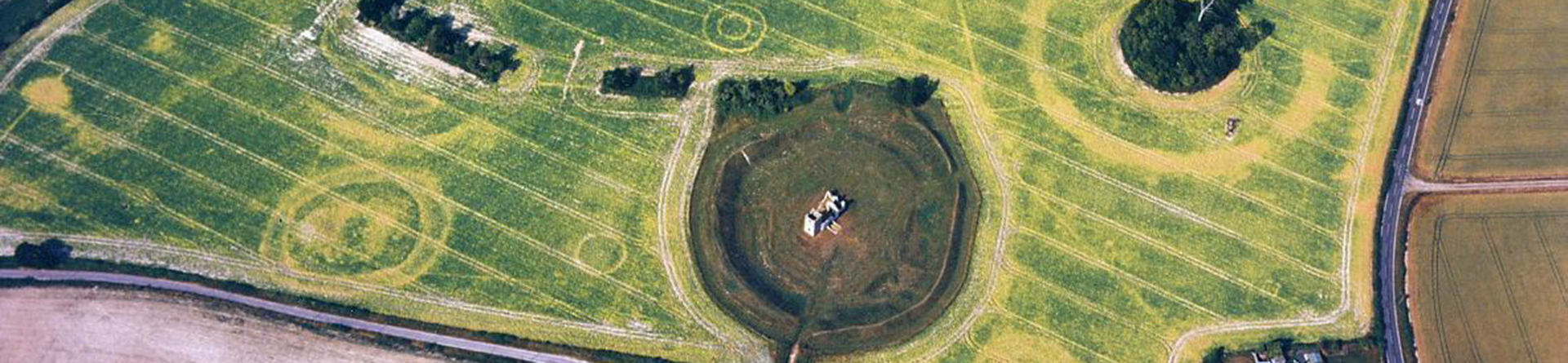 Colour aerial photograph of fields in crop with a ruined church sitting within an earthwork bank