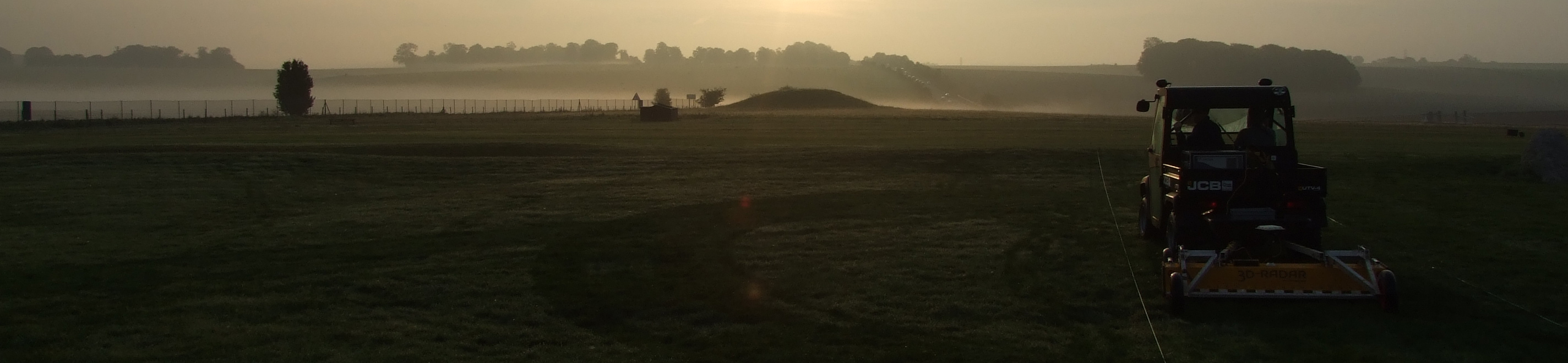 Colour photograph showing a misty landscape with a small buggy towing a low yellow "truck" near the right hand edge
