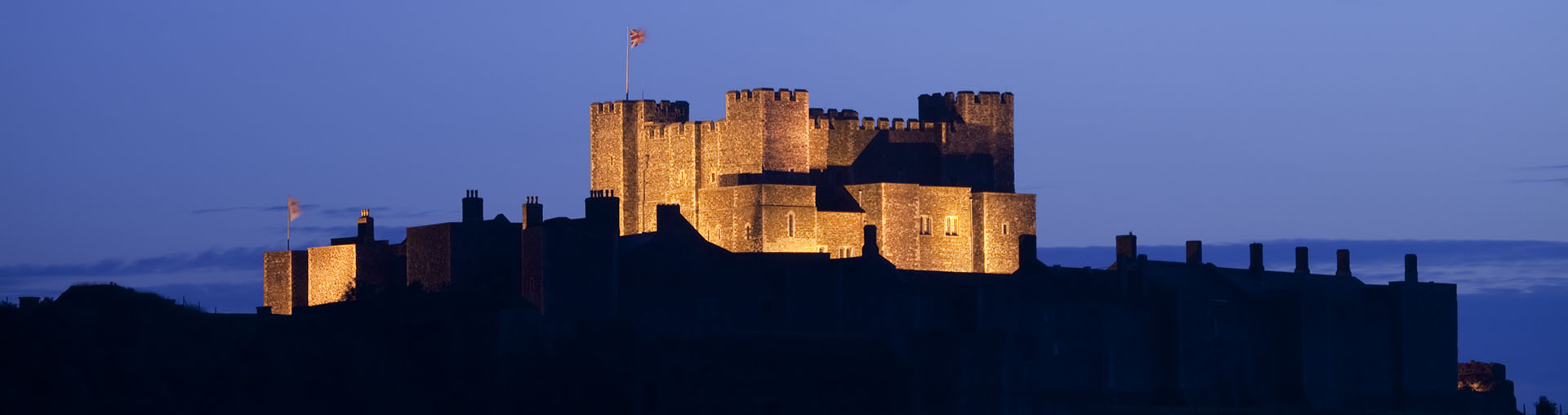 A large medieval castle keep dramatically floodlit at twilight.