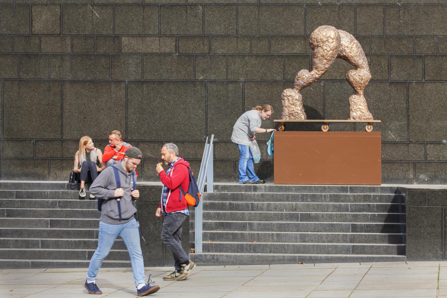 Five people in a street setting containing steps and a Henry Moore sculpture