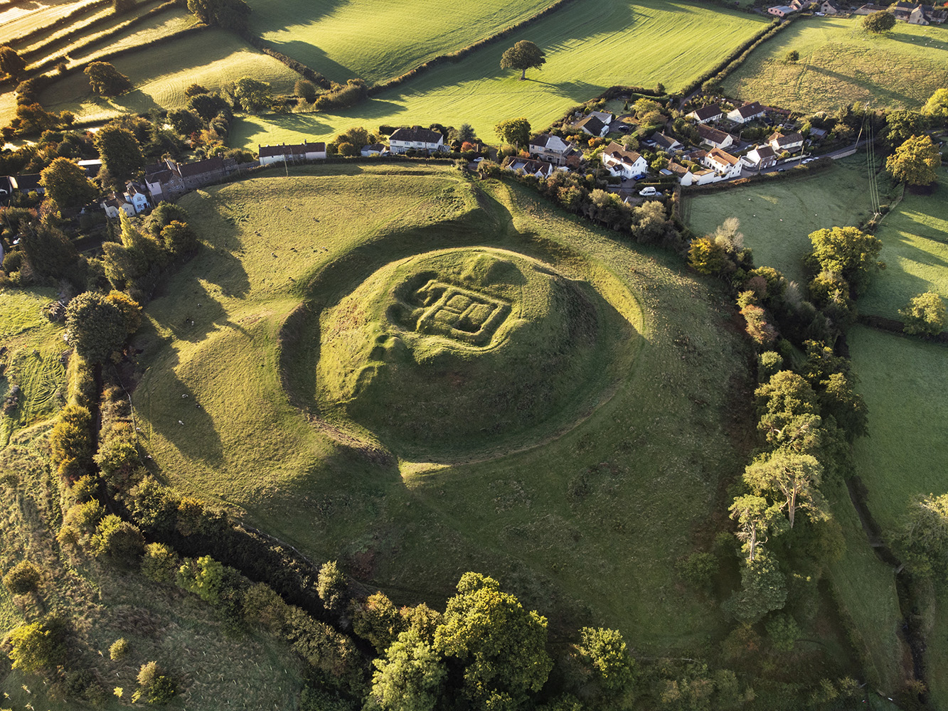 Aerial view of the earthworks of motte and baileys, and adjacent village.