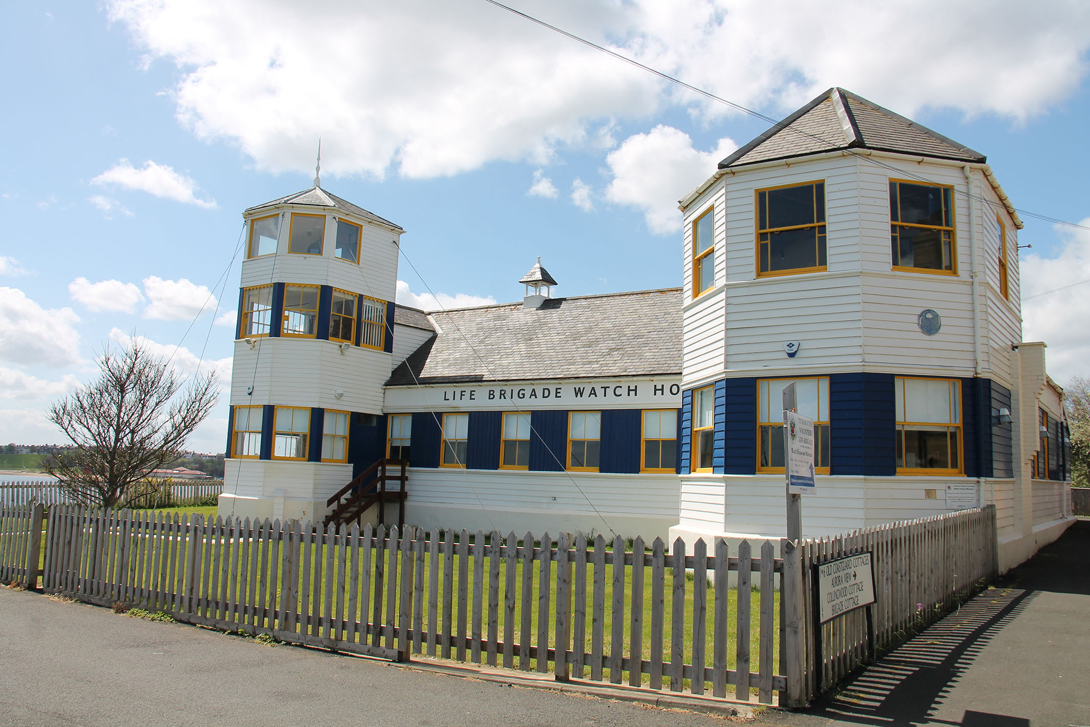 Photo of the outside of the Life Brigade Watch House - a white wooden building with blue and yellow painted windows.
