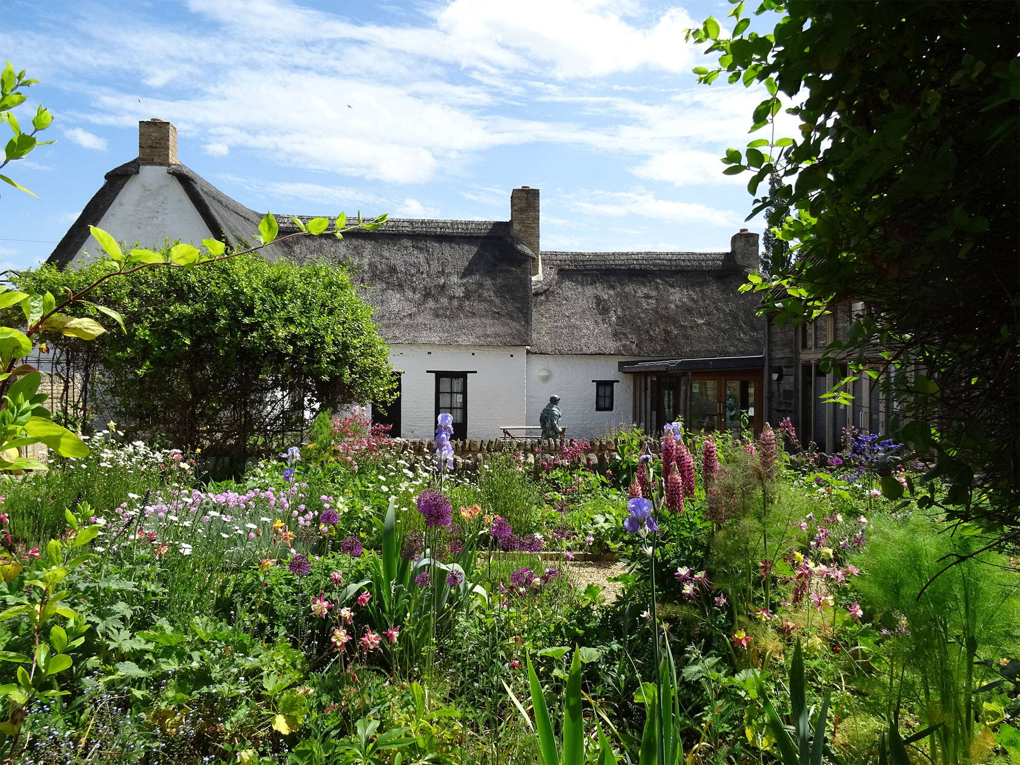 The photograph shows a white cottage with thatched roof and country garden in bloom 