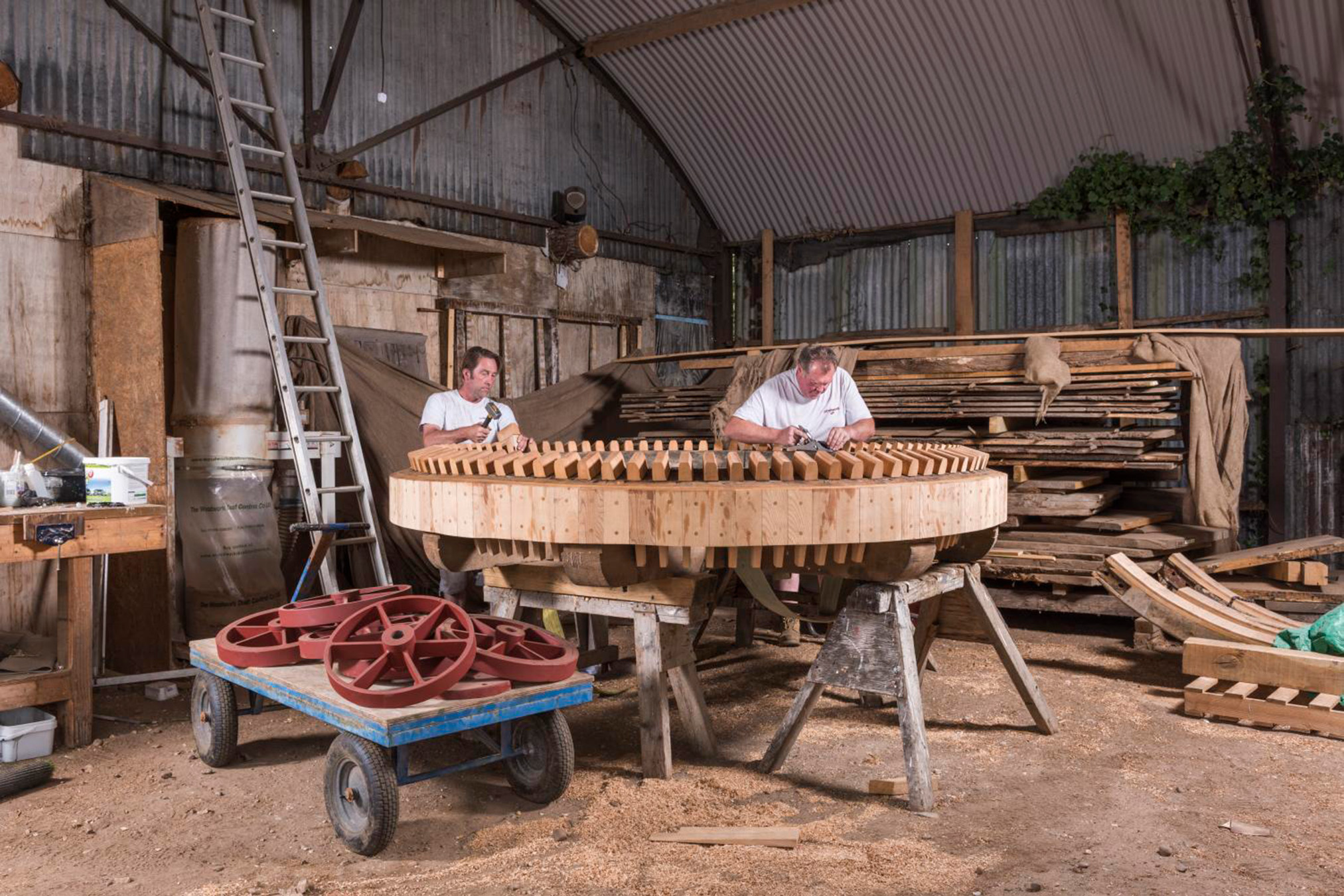 Interior view of a restorers' workshop, showing two male restorers working on a mill's new brake wheel