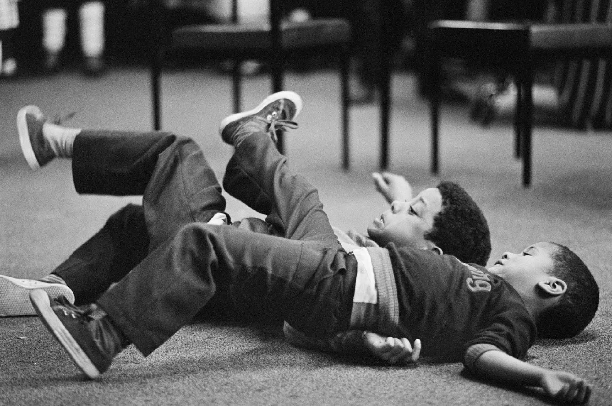 Two young boys playfighting on the floor. 