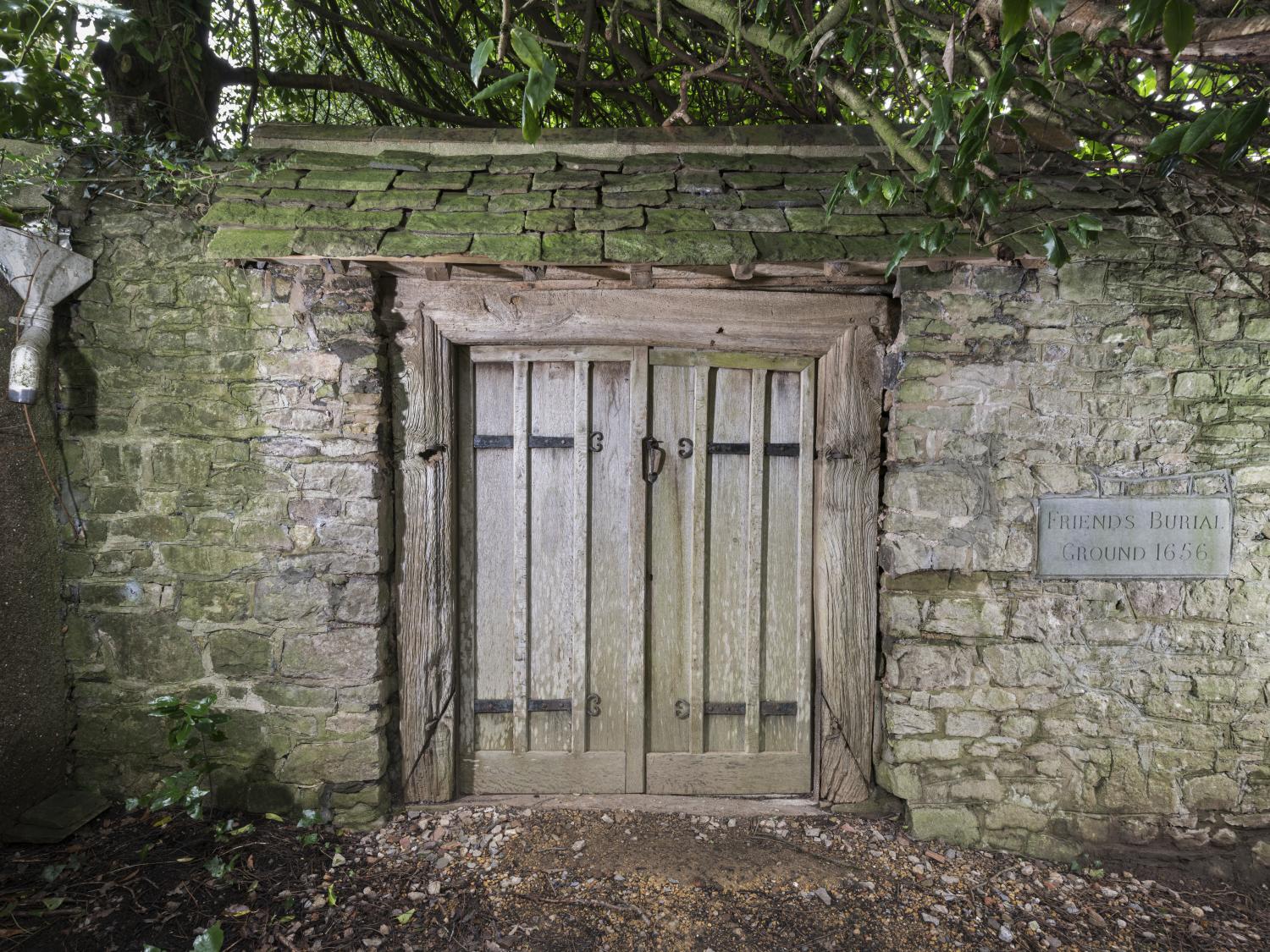 A photograph of a stone wall with an old wooden door. Beside the door a plaque reads Friends Burial Ground, 1656.