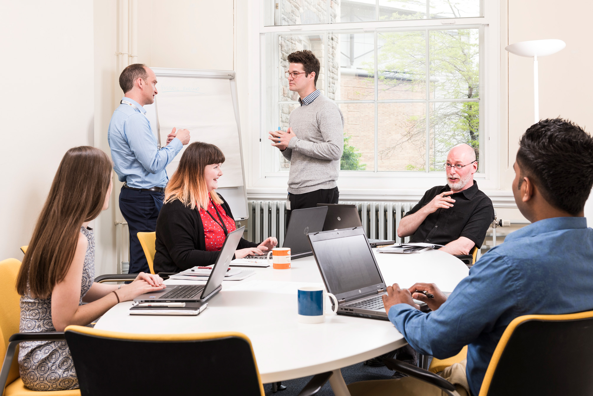 Several people of different ages, genders and backgrounds around a table in an office meeting room