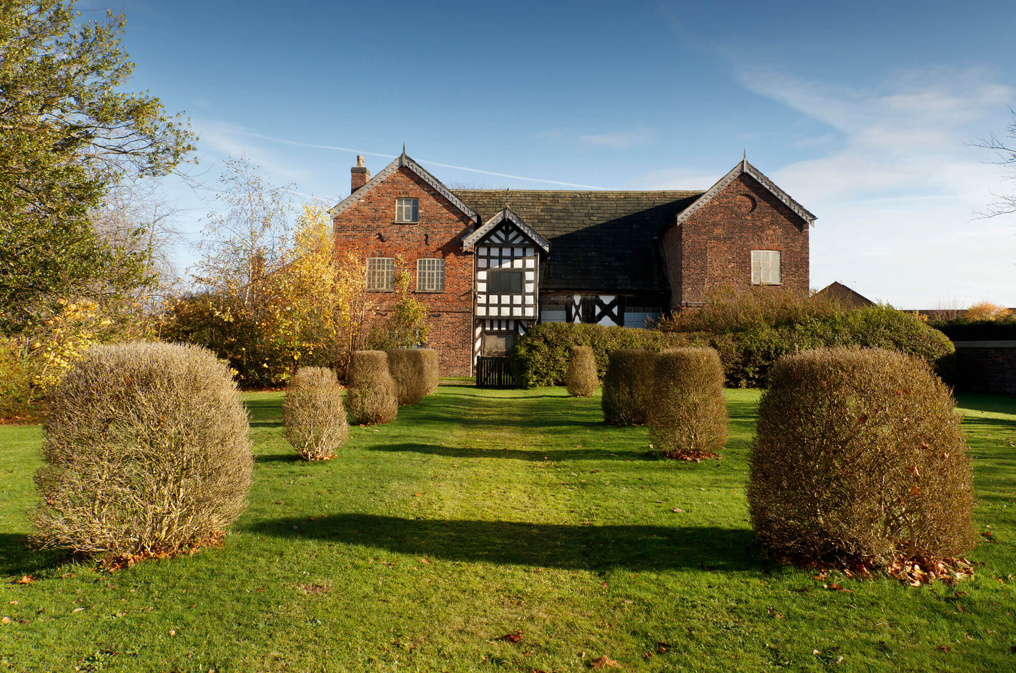 A red brick and timber-framed building with a garden in the foreground.