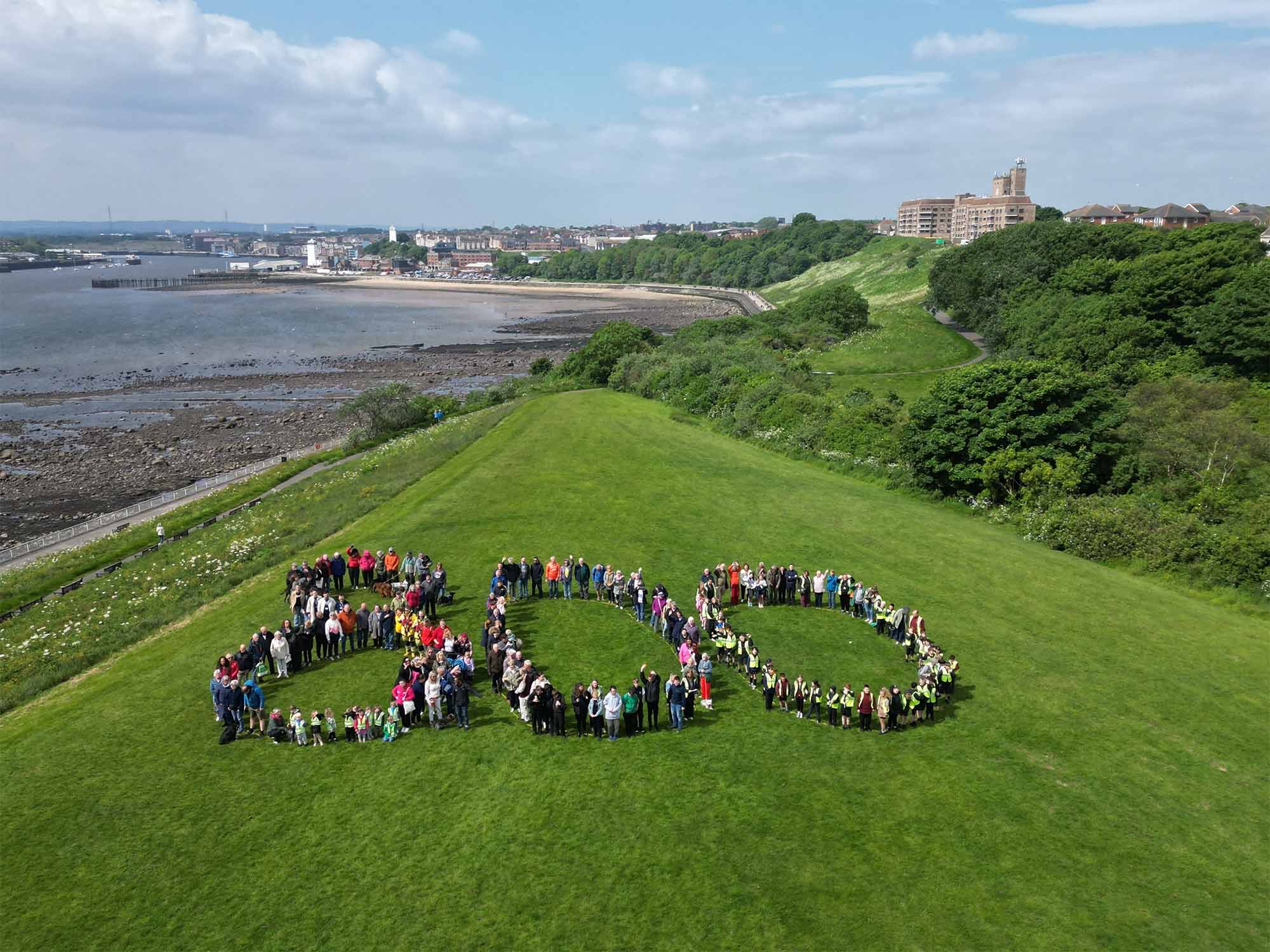 A large group of people standing on a grassy slope in the shape of a large number eight hundred