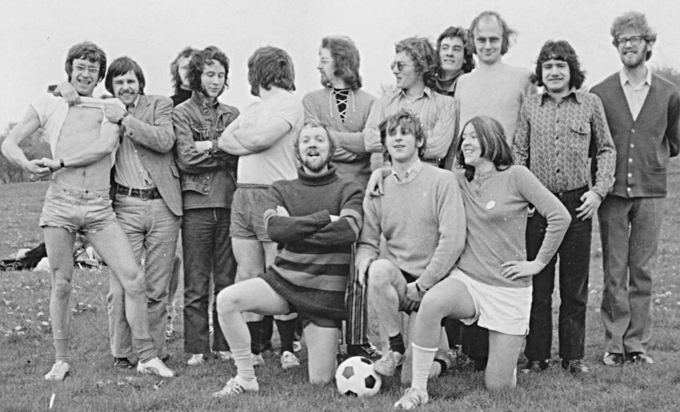 Black and white photo of a group of young men and one woman in high spirits posing for a post-match photo.