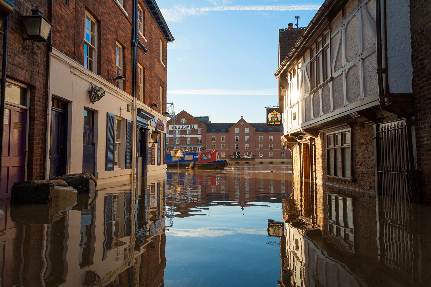 Flood water between buildings in a street, with a wider expanse of water beyond.