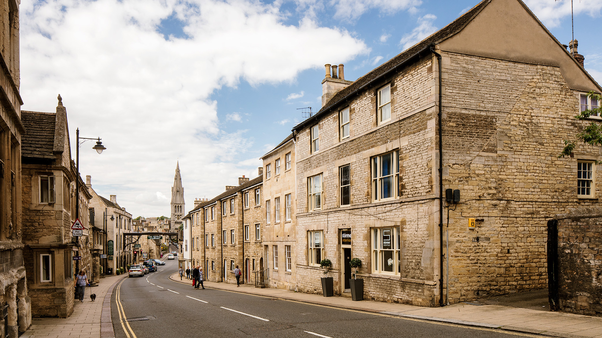 Looking down a street bordered by stone buildings with a church tower in the distance