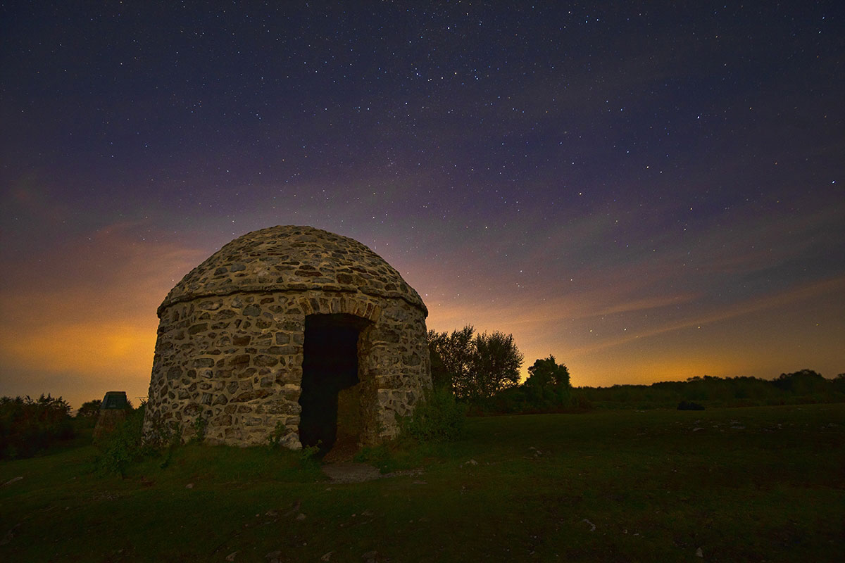 Alt text: A beehive shaped stone building photographed against a starry night sky.