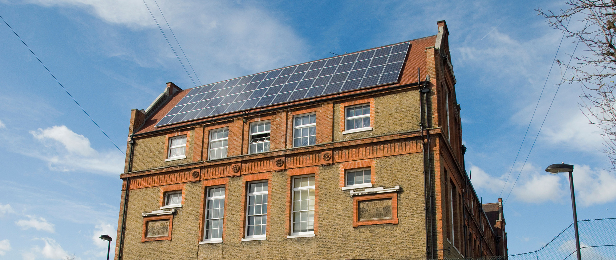 Solar panels on the red tile roof of a brick building.