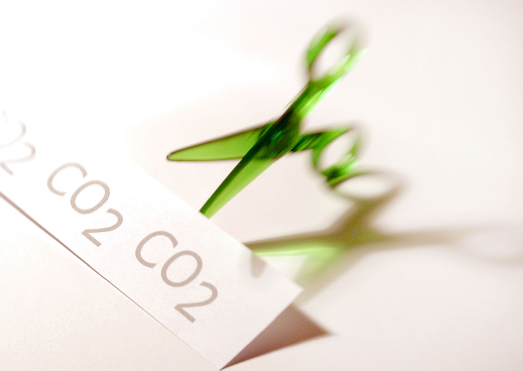 A symbolic image of cutting carbon emissions represented by a pair of scissors  cutting  through a sign that has CO2 written on it.
