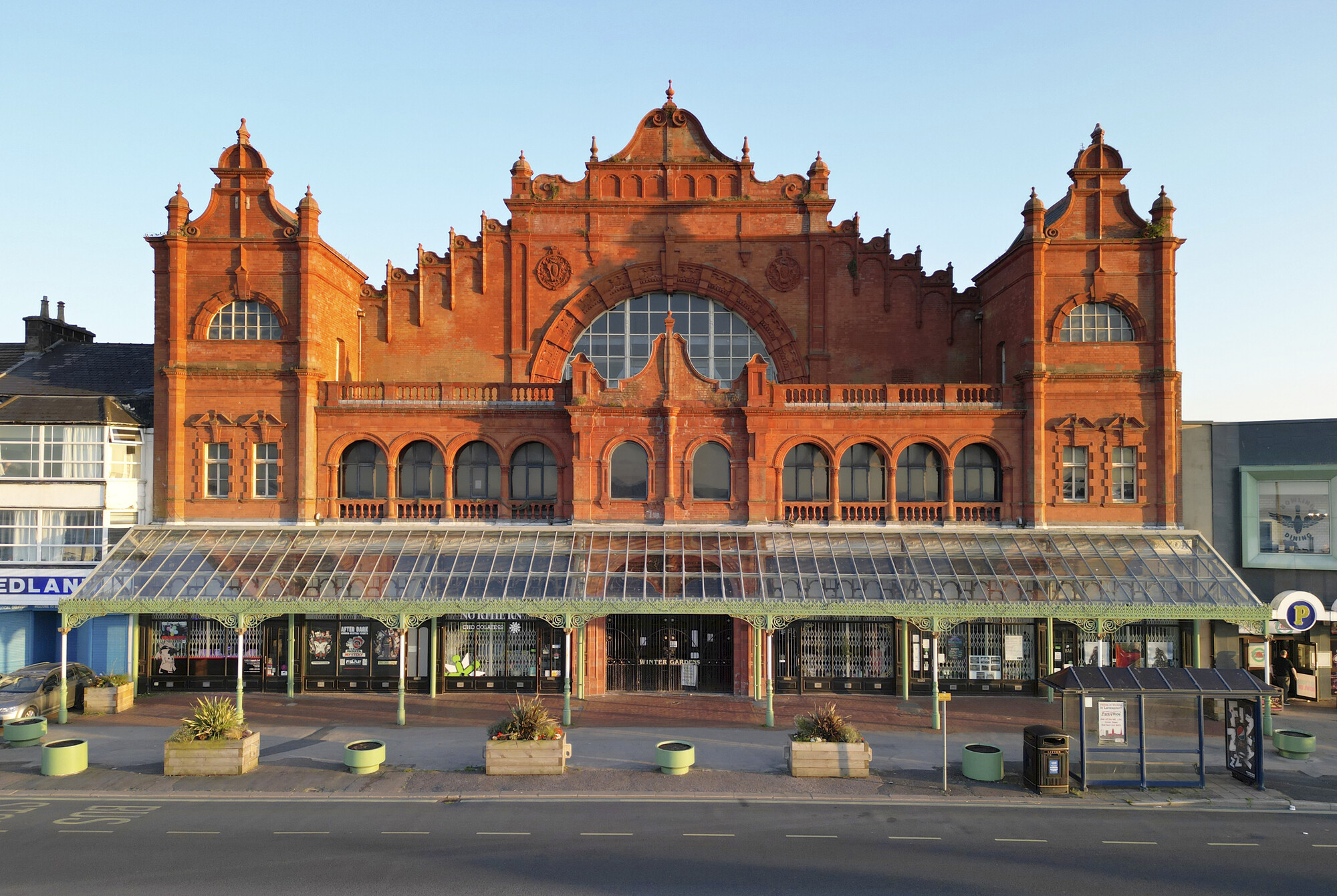 Colour photograph of a large ornate red brick building with wrought iron and glass canopy to street level.