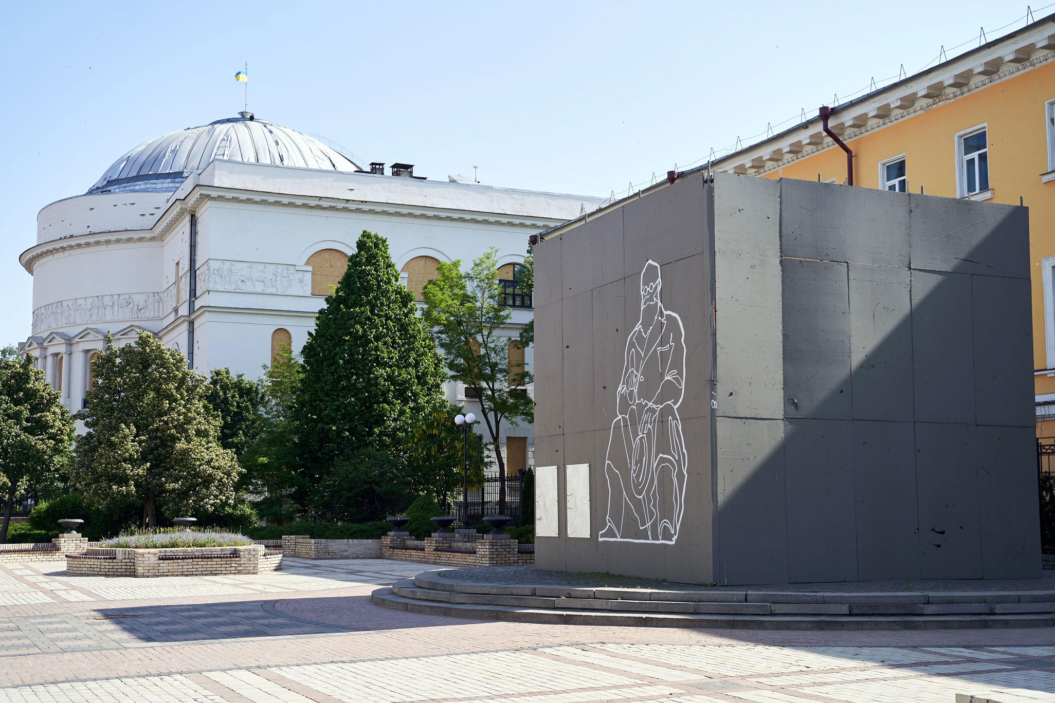 A Ukrainian monument which has been encased to prevent war damage; on the outside of the casing is an outline picture of a seated statesman, illustrating the statue beneath.